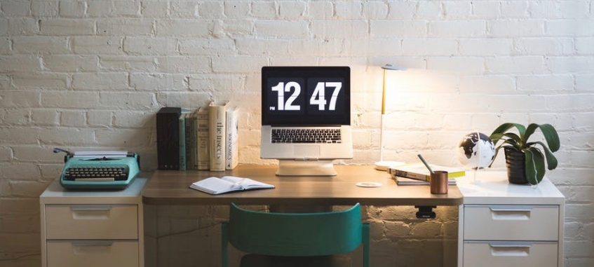 a clock, books, and a typewriter on a wooden table