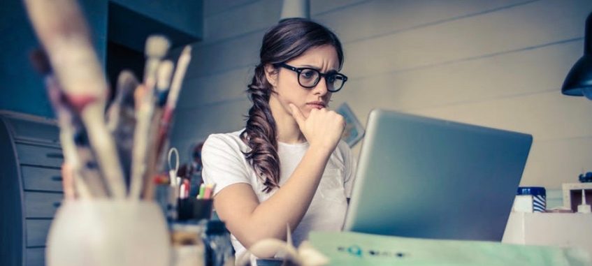 a girl in glasses sitting at the deak looking at the screen