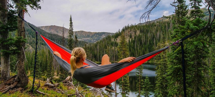 a girl is lying in a hammock admiring the mountains