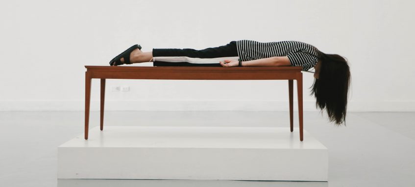 a girl lying on the table looking down the floor in a white room