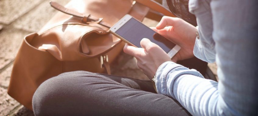 a girl scrolling feed in her phone sitting on the ground