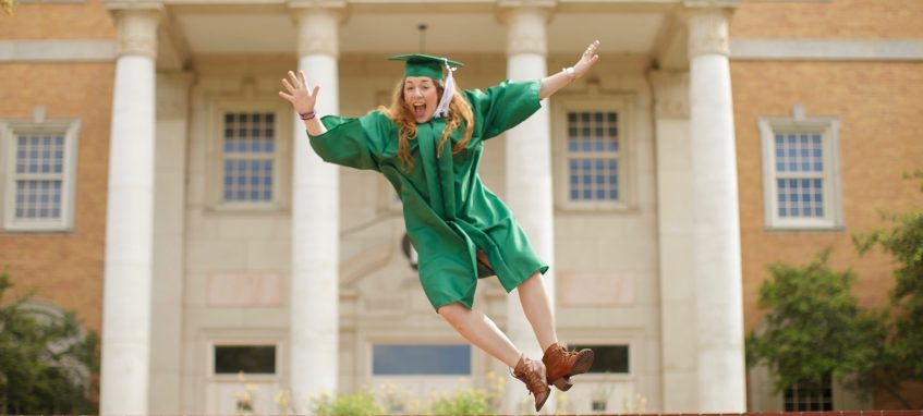 a graduate girl jumping up near the university