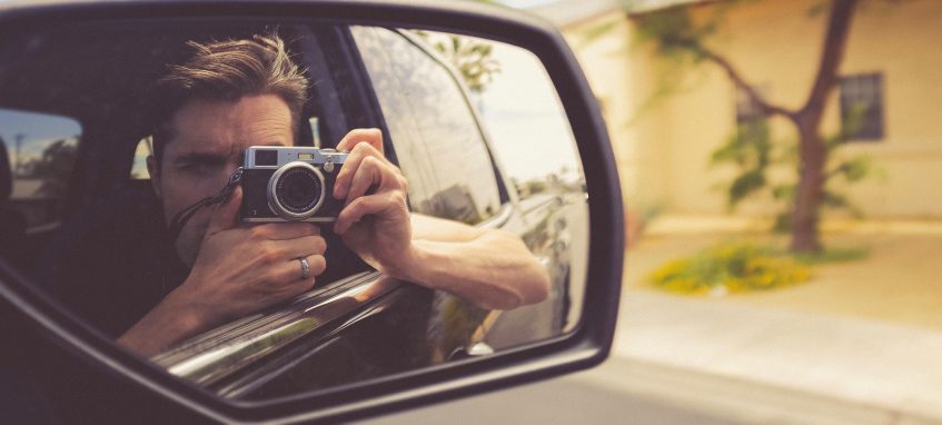 a man taking photo of his reflection in the car mirror