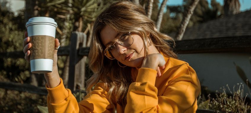 a model in yellow sweater and holding a cup of coffee to go