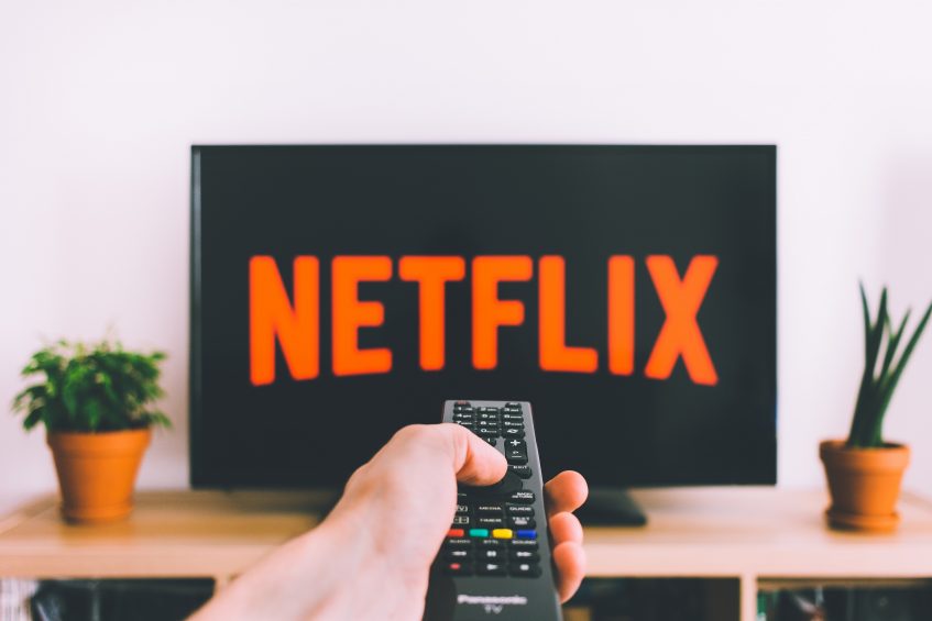 a person pointing a remote control towards the screen with a sign Netflix