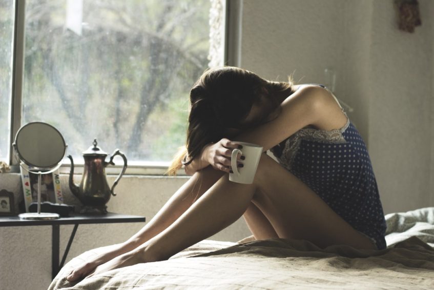 a depressed girl sitting on the bed with a cup of tea in her hands