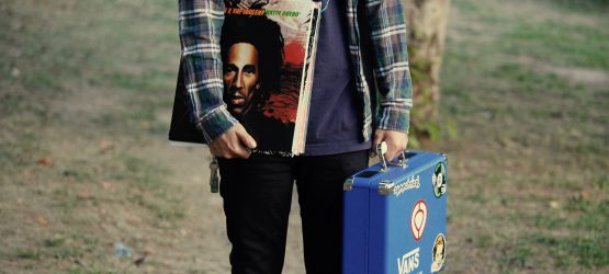a student wearing a plaid shirt holds a briefcase and vinyl records