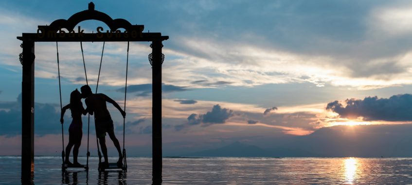 a young couple kissing on swings in the middle of the sea at sunset