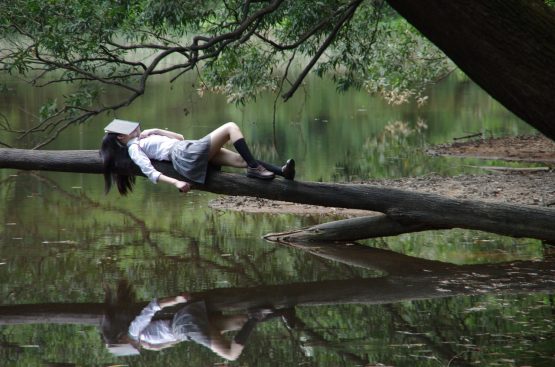 a girl lying near the river bank with a book on her face