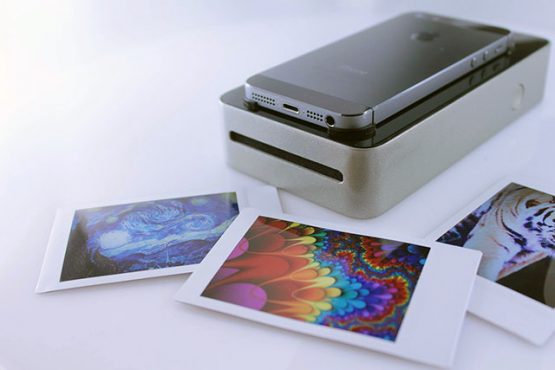 an instant photo portable printer with an iphone on it, and three colorful picters