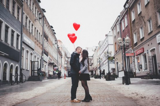 a couple standing in the middle of the street kissing with heart balloons in their hands