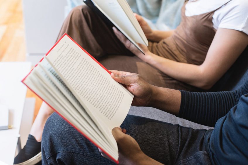 a guy and a girl are reading books sitting on a couch