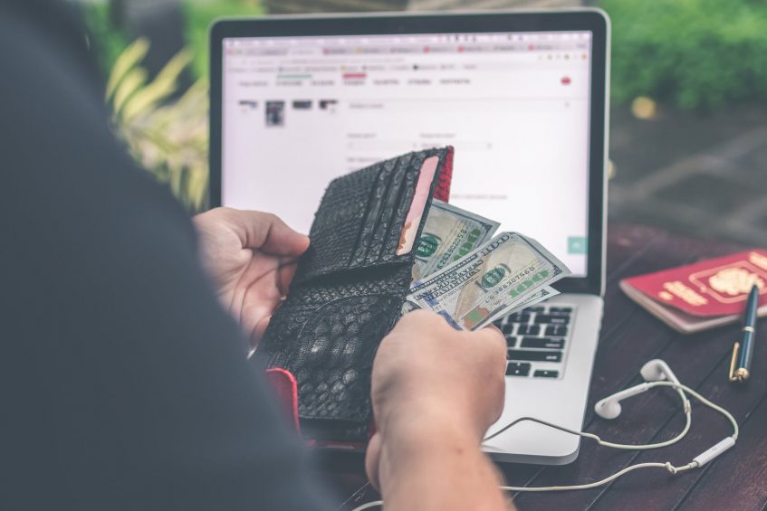 a guy holding a wallet with money in front of a laptop