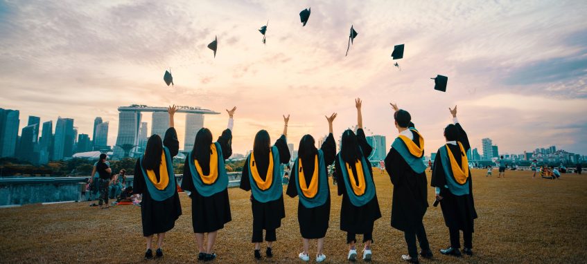 students throwing their graduate caps up on a lawn