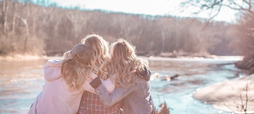 three women hug each other sitting at the river