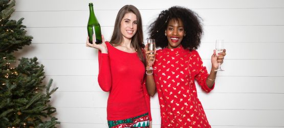 two girls with a bottle of champagne stand near a Christmas tree