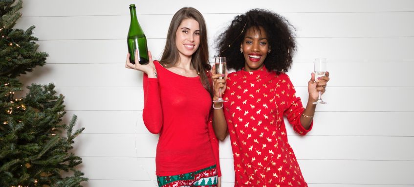 two girls with a bottle of champagne stand near a Christmas tree