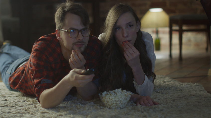 young couple lays on the floor watching a movie and eating popcorn