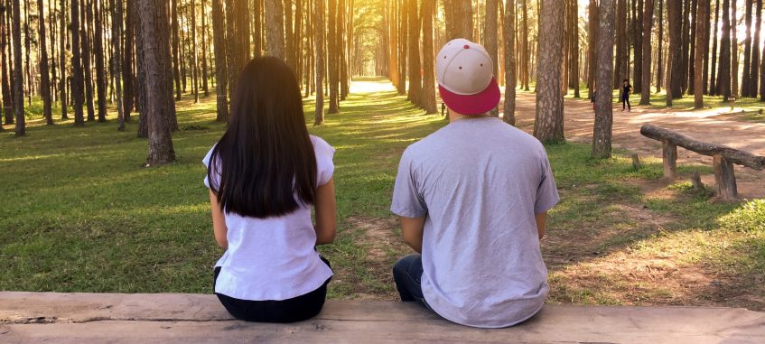 young couple sitting on the bench in the wood