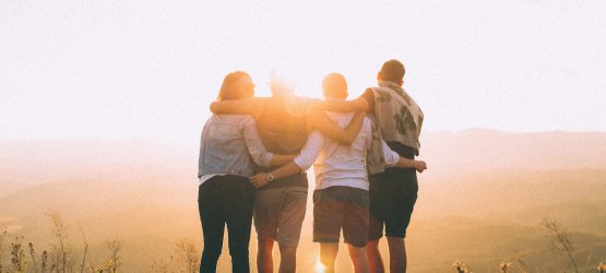 young people stand in a row, hug each other and look at sunset